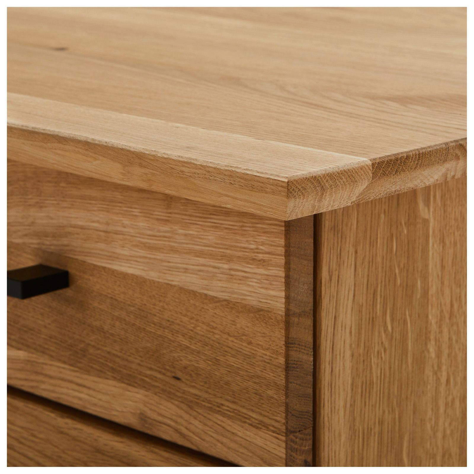 Nahaufnahme einer Ecke eines Schreibtisches aus Holz mit sichtbarer Maserung und einer Schublade mit schwarzem Griff, Perspektive von oben.