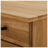 Nahaufnahme einer Ecke eines Schreibtisches aus Holz mit sichtbarer Maserung und einer Schublade mit schwarzem Griff, Perspektive von oben.