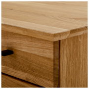 Nahaufnahme einer Ecke eines Schreibtisches aus Holz mit sichtbarer Maserung und einer Schublade mit schwarzem Griff, Perspektive von oben.