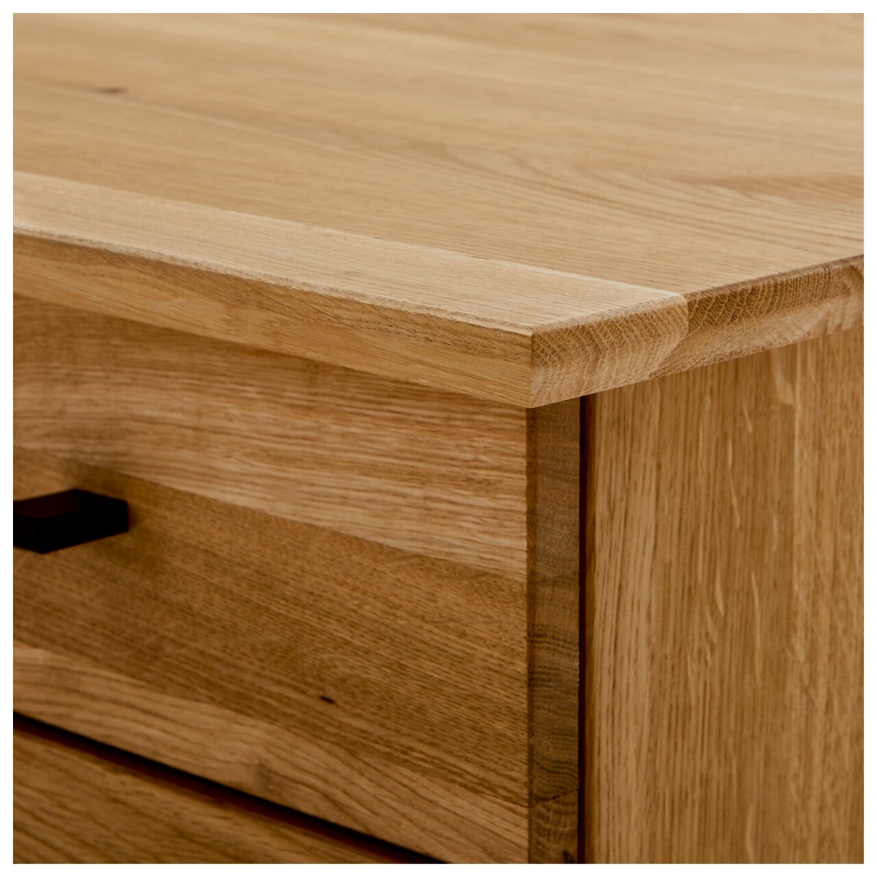 Close-up van een hoek van een houten bureau met zichtbare nerf en een lade met een zwarte handgreep, gezien van bovenaf.