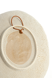 Rückseite eines cremefarbenen Keramiktellers mit Craquelé-Glasur und ovalem Aufhänger mit brauner Kordel, Nahaufnahme in Draufsicht