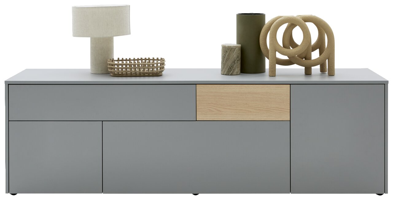 Modernes TV-Lowboard in Grau mit Holzdetails, dekoriert mit einer Tischlampe, einem Korb und Vasen, Frontalansicht.