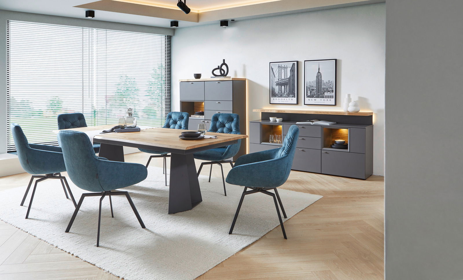 Moderner Esstisch mit Holzplatte und dunklem Gestell, umgeben von blauen Polsterstühlen in einem stilvollen Esszimmer mit großen Fenstern, seitliche Perspektive.