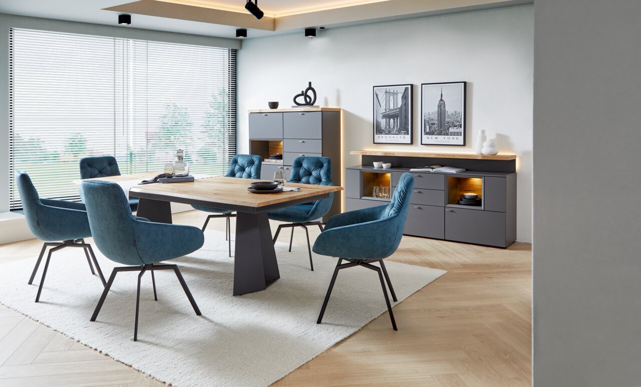 Moderner Esstisch mit Holzplatte und dunklem Gestell, umgeben von blauen Polsterstühlen in einem stilvollen Esszimmer mit großen Fenstern, seitliche Perspektive.