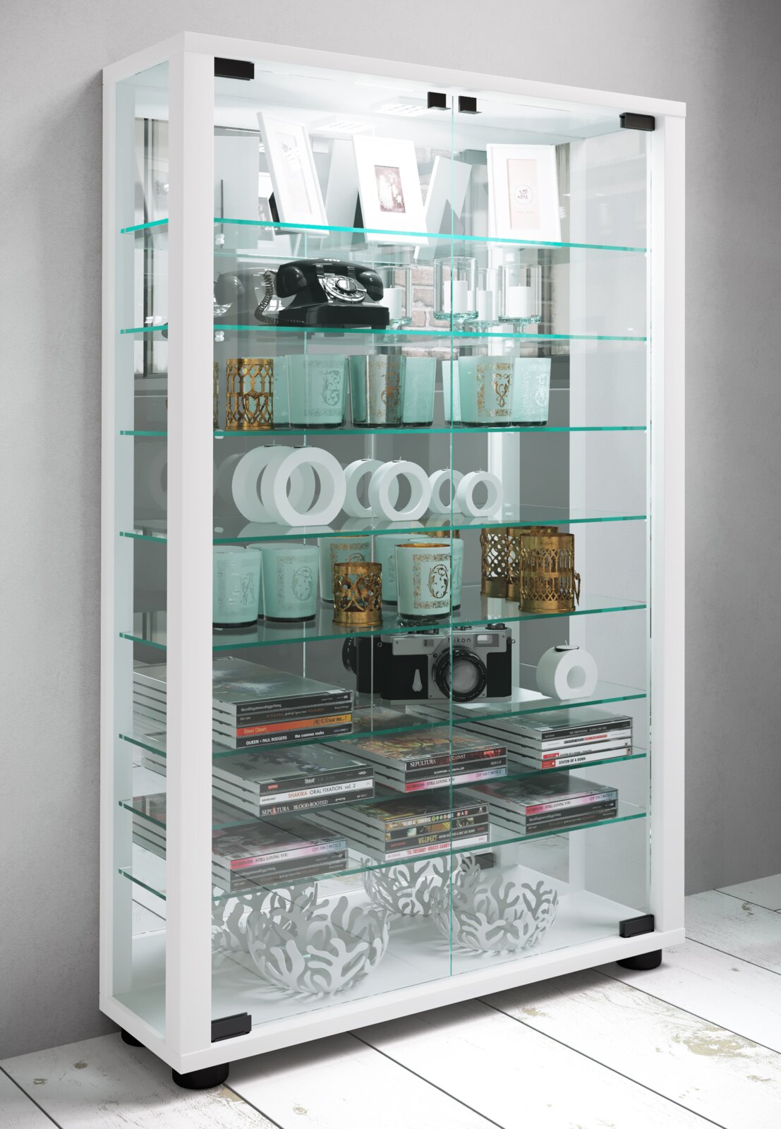 Weiße Glasvitrine mit Glasböden und transparenten Schiebetüren, gefüllt mit Dekoartikeln, CDs und Kamera; Perspektive: frontale Ansicht mit leichtem Blick von links oben.