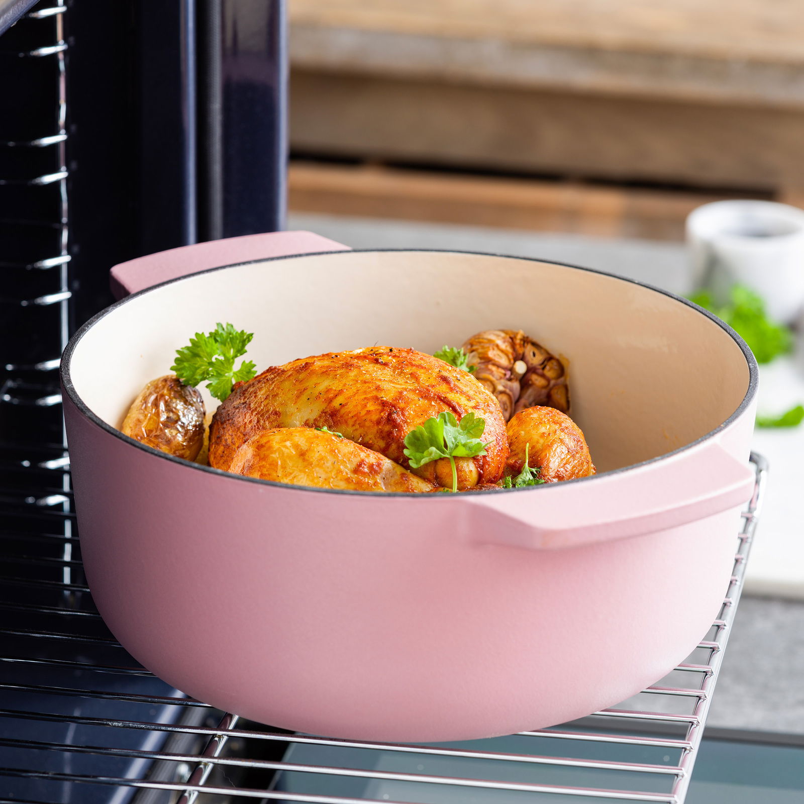 Runder Gusseisen Bräter in Rosa mit gebratenem Hähnchen und Gemüse, seitliche Perspektive im Ofen.
