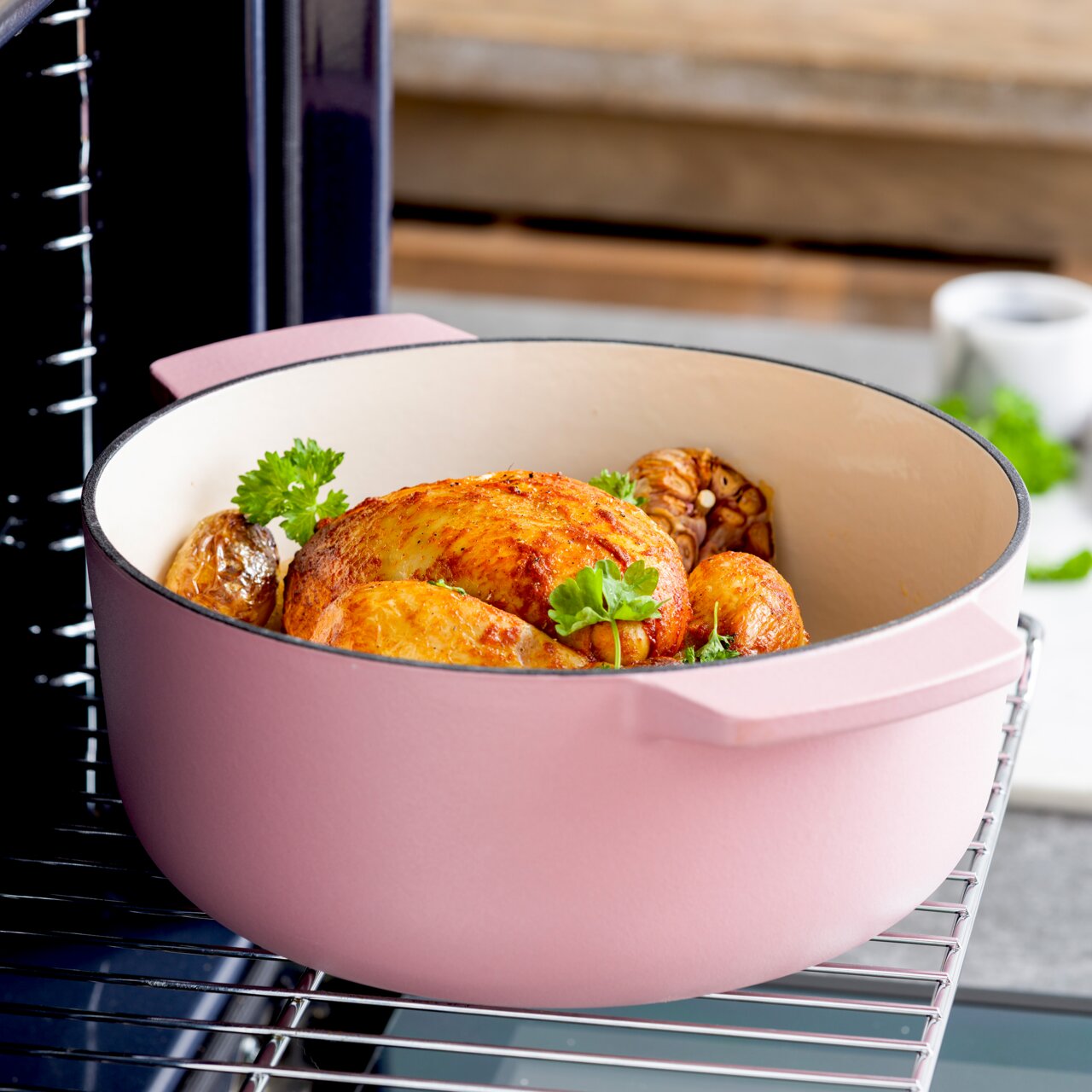 Runder Gusseisen Bräter in Rosa mit gebratenem Hähnchen und Gemüse, seitliche Perspektive im Ofen.