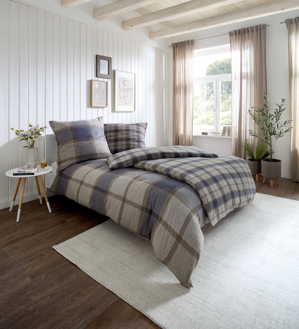Gemütliches Schlafzimmer mit kariertem Bettwäsche-Set in Blau- und Beigetönen, seitliche Perspektive auf das Bett, helle und einladende Atmosphäre mit natürlichem Licht.