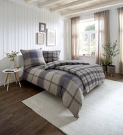 Gemütliches Schlafzimmer mit kariertem Bettwäsche-Set in Blau- und Beigetönen, seitliche Perspektive auf das Bett, helle und einladende Atmosphäre mit natürlichem Licht.