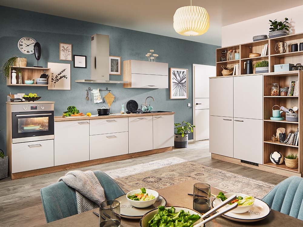 Moderne Küche in Beige und Holzoptik mit blauer Wand, offenen Regalen, Deko-Elementen und Essbereich.