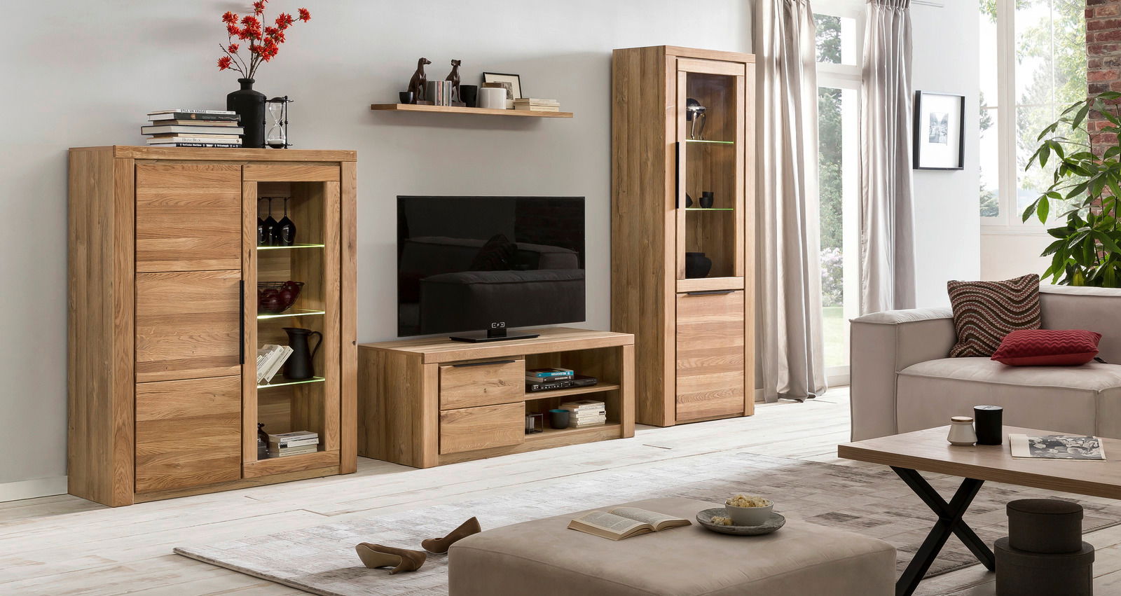 Wohnzimmer mit modernen Holzmöbeln, darunter ein TV-Lowboard, eine Vitrine und ein Highboard, aus der Perspektive von vorne betrachtet.