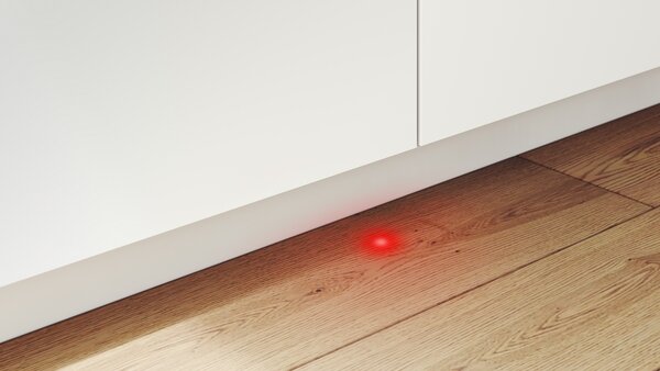 Rote Lichtanzeige auf dem Boden vor einem eingebauten Geschirrspüler, Perspektive von vorne.