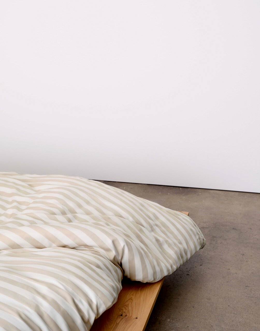 Bettwäsche mit beige-weißen Streifen auf einem Holzbett, seitliche Perspektive