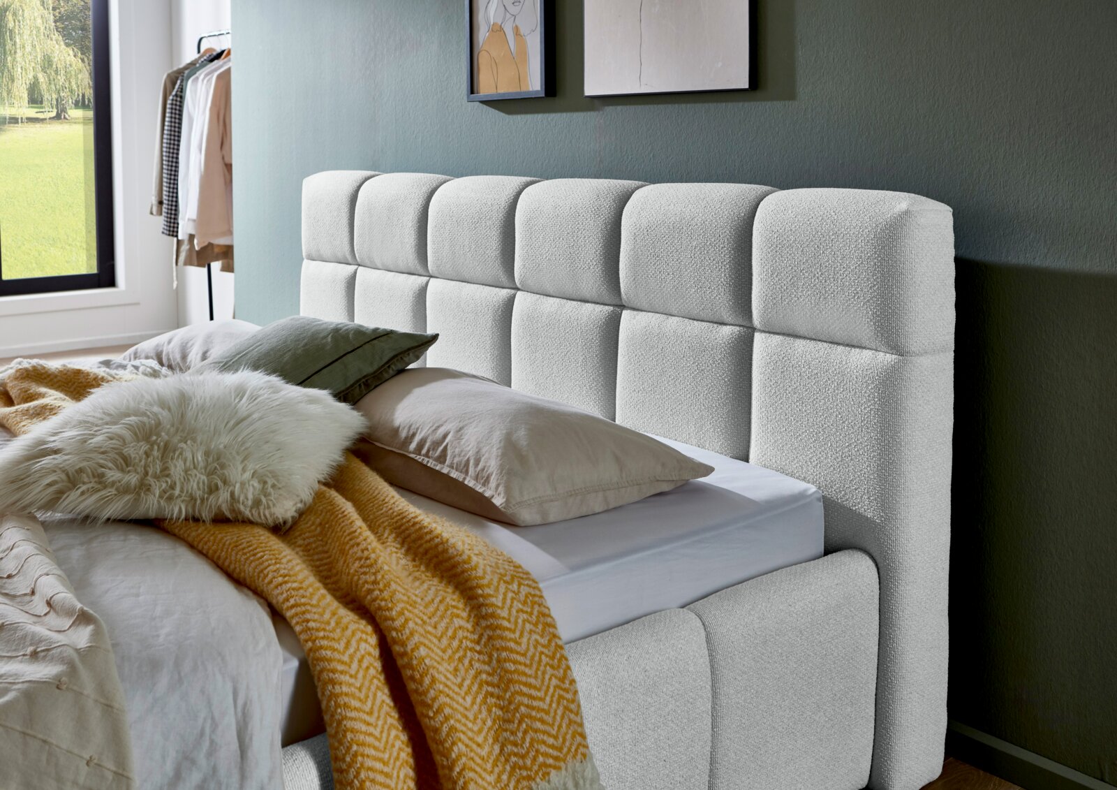 Modern gestoffeerd bed met gestoffeerd hoofdeinde, gezien vanaf de zijkant, versierd met kussens en een deken in een stijlvolle slaapkamer.