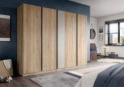 Großer Kleiderschrank in heller Eichenholz-Optik mit vier Türen und mittlerer Spiegeltür, in einem modern eingerichteten Schlafzimmer, perspektivische Frontansicht leicht von links.