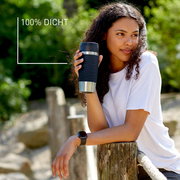 Frau hält einen schwarzen MUG Classic Wave 0,36L Becher, seitliche Perspektive, im Freien, mit der Aufschrift '100% DICHT'.