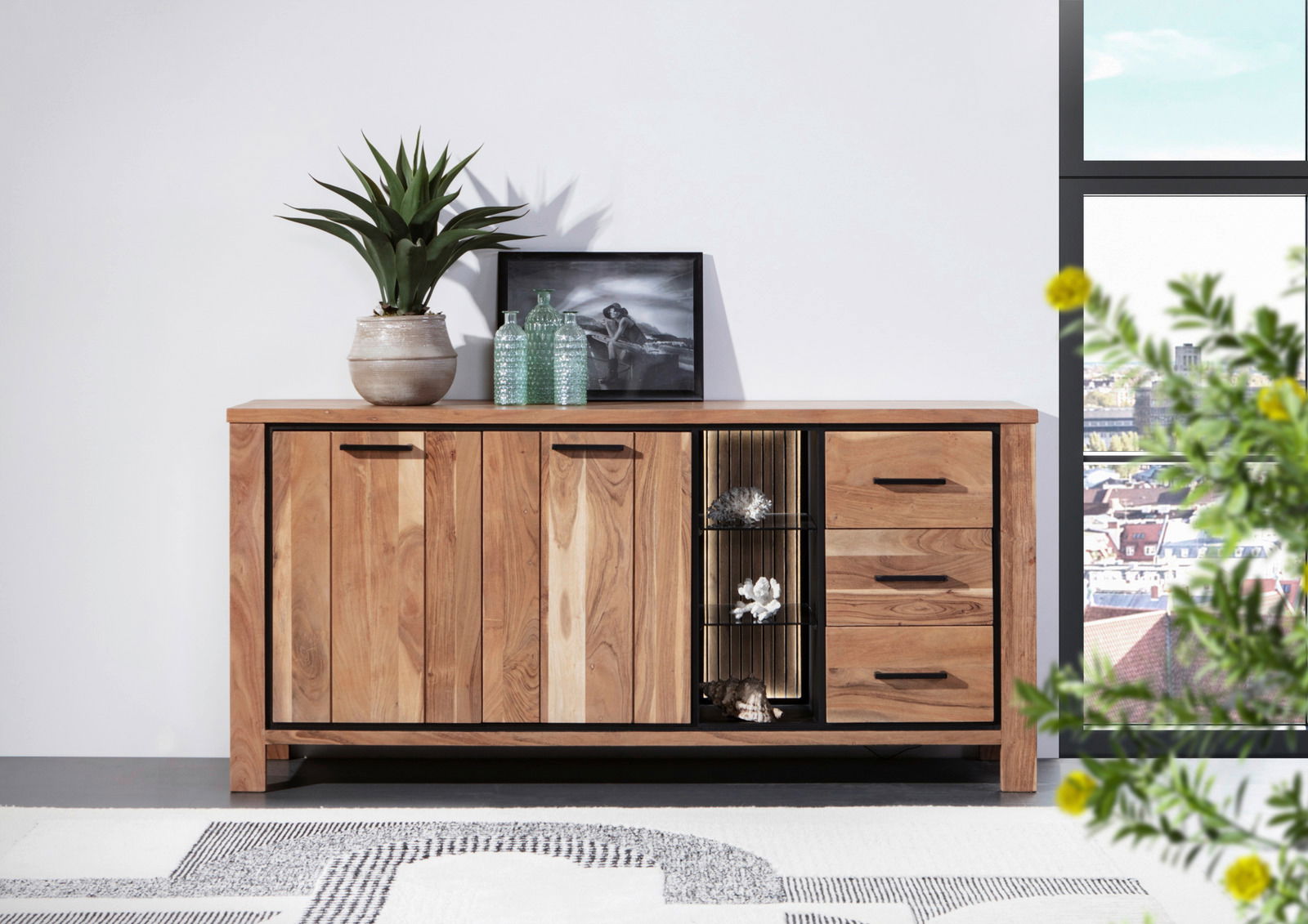 Landscape Sideboard AKAZIO Holz-Sideboard mit drei Türen und drei Schubladen, dekoriert mit Pflanzen und Glasflaschen, aus frontaler Perspektive fotografiert.