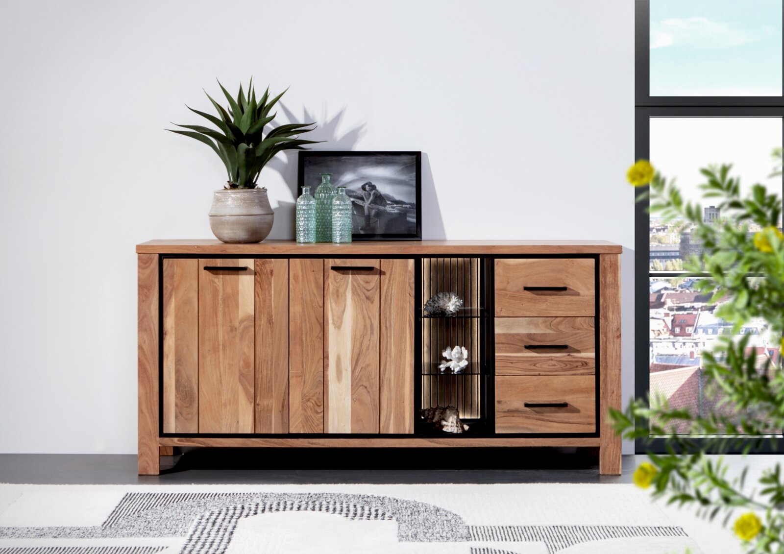 Landscape Dressoir AKAZIO Holz-Sideboard mit drei Türen und drei Schubladen, dekoriert mit Pflanzen und Glasflaschen, aus frontaler Perspektive fotografiert.