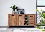 Houten dressoir met drie deuren en drie lades, versierd met planten en glazen flessen, gefotografeerd vanuit een vooraanzicht.