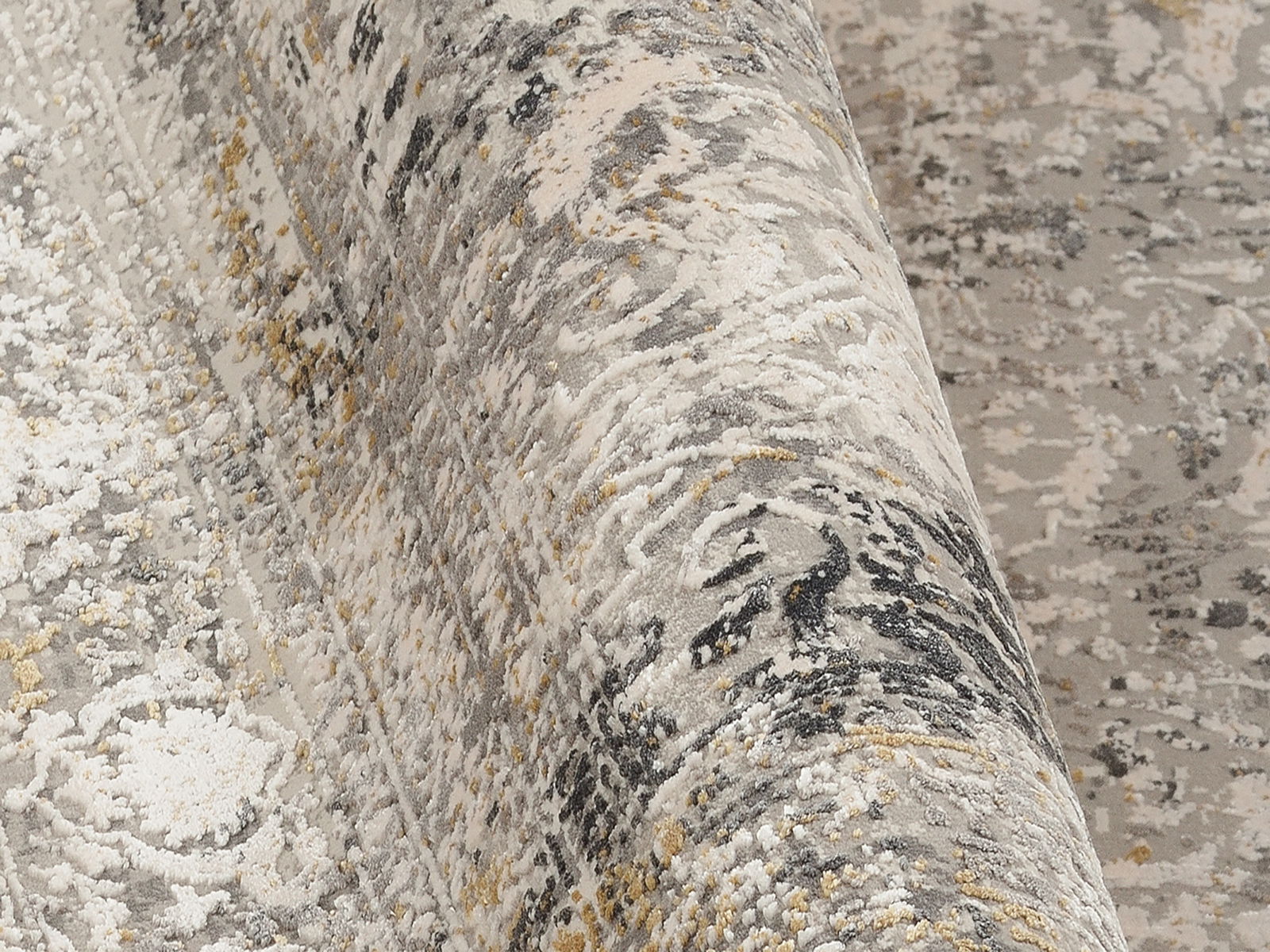 Nahaufnahme eines Designer-Teppichs mit abstraktem Muster in Grau- und Beigetönen, teilweise aufgerollt.