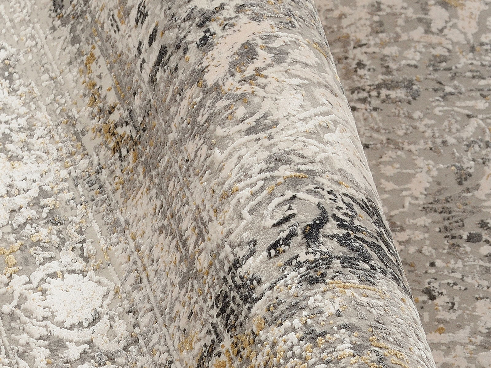 Nahaufnahme eines Designer-Teppichs mit abstraktem Muster in Grau- und Beigetönen, teilweise aufgerollt.