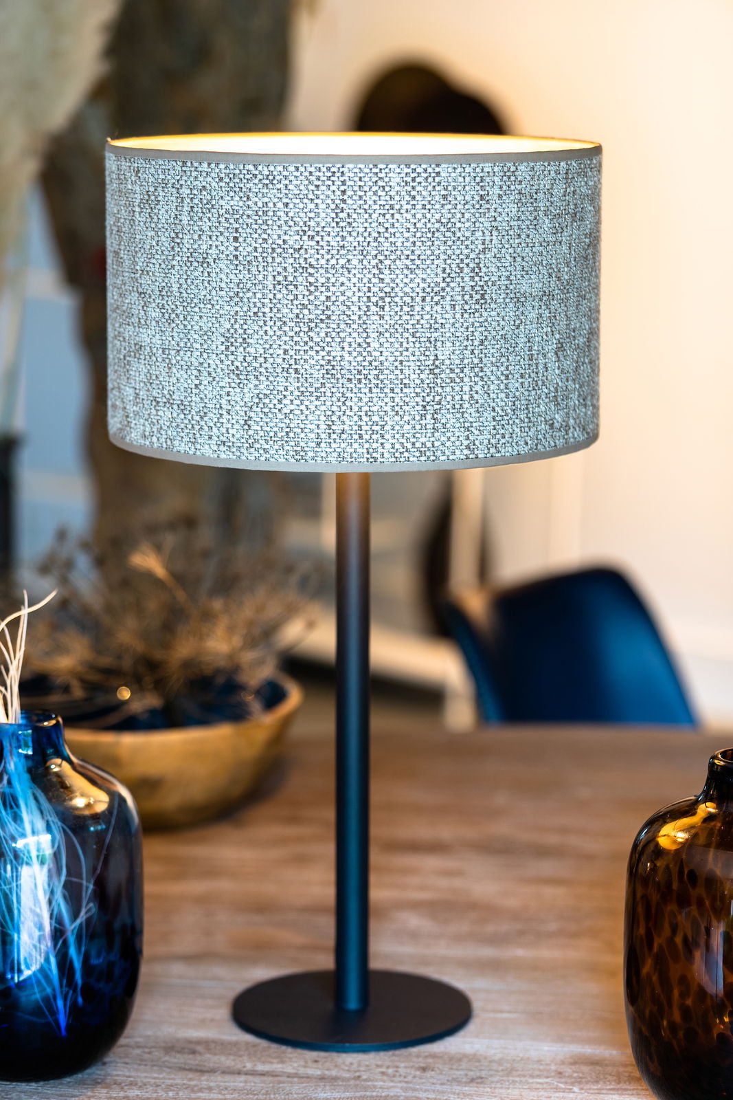 Moderner Lampenfuß mit schwarzem Ständer und rundem, texturiertem Lampenschirm, seitliche Perspektive auf einem Holztisch mit dekorativen Vasen.