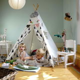 Kinder spielen in einem Tipi-Zelt mit Baum-Muster in einem hellen Raum. Perspektive von vorne.
