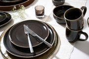 Elegantes Geschirrset in dunklen Tönen mit Tellern, Tassen und Schalen, von oben betrachtet, auf einem weißen Tischtuch arrangiert.