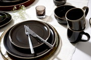 Elegantes Geschirrset in dunklen Tönen mit Tellern, Tassen und Schalen, von oben betrachtet, auf einem weißen Tischtuch arrangiert.