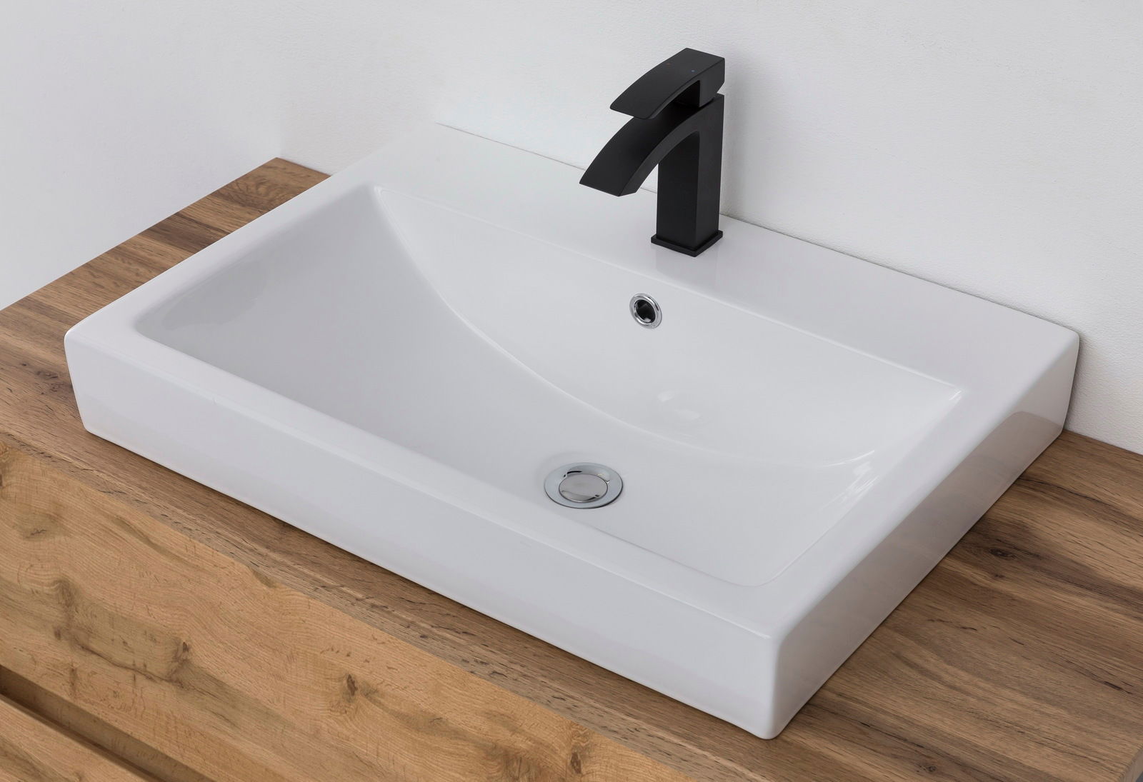Moderner Waschtisch mit rechteckigem, weißem Becken und schwarzem Wasserhahn, aus der Vogelperspektive auf einer Holzoberfläche.