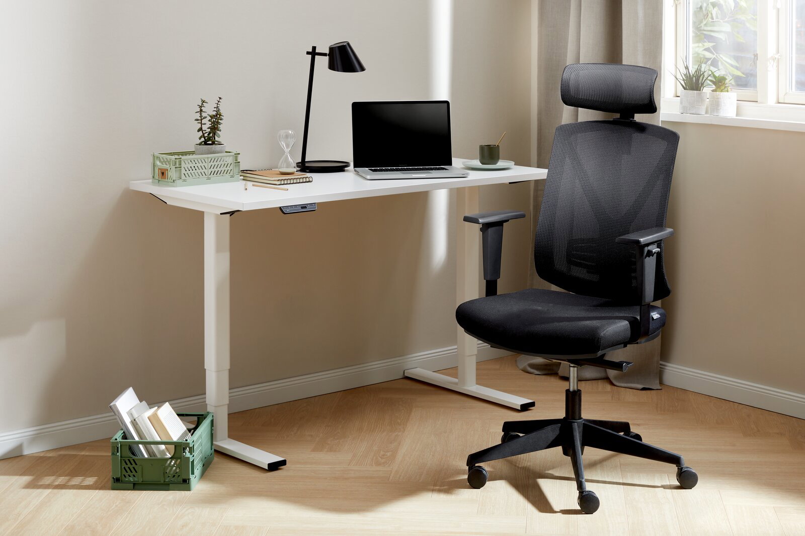 Moderner E-Schreibtisch mit weißer Tischplatte und höhenverstellbaren Beinen, ausgestattet mit einem Laptop, einer Lampe und Pflanzen, aus seitlicher Perspektive fotografiert.