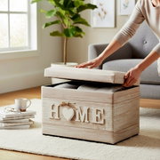 Hellholzfarbene Aufbewahrungsbox/Sitztruhe mit Schriftzug „HOME“ wird in einem Wohnzimmer von schräg vorn oben geöffnet, Decke im Inneren sichtbar.