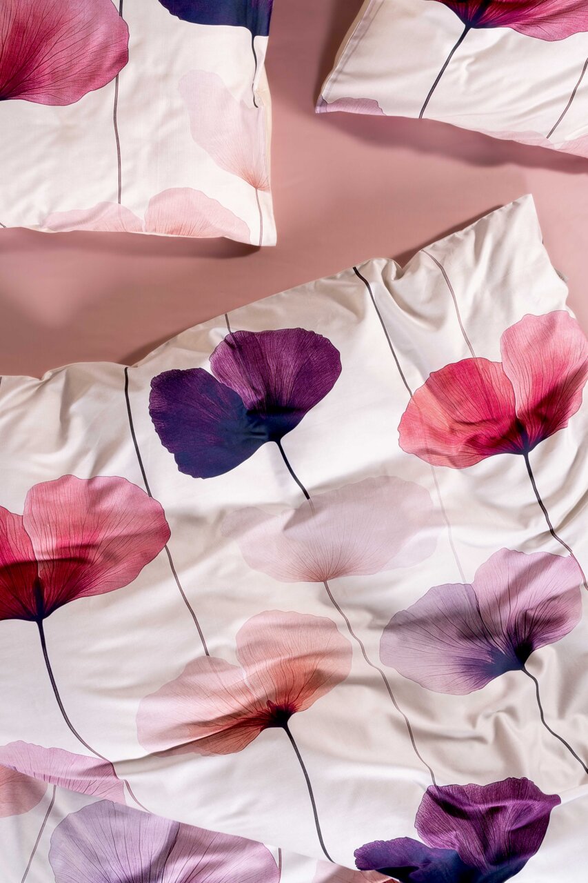 Beddengoedset met witte achtergrond en grote bloemenprint in roze, paars en rood, met roze hoeslaken, bovenaanzicht