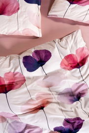 Beddengoedset met witte achtergrond en grote bloemenprint in roze, paars en rood, met roze hoeslaken, bovenaanzicht