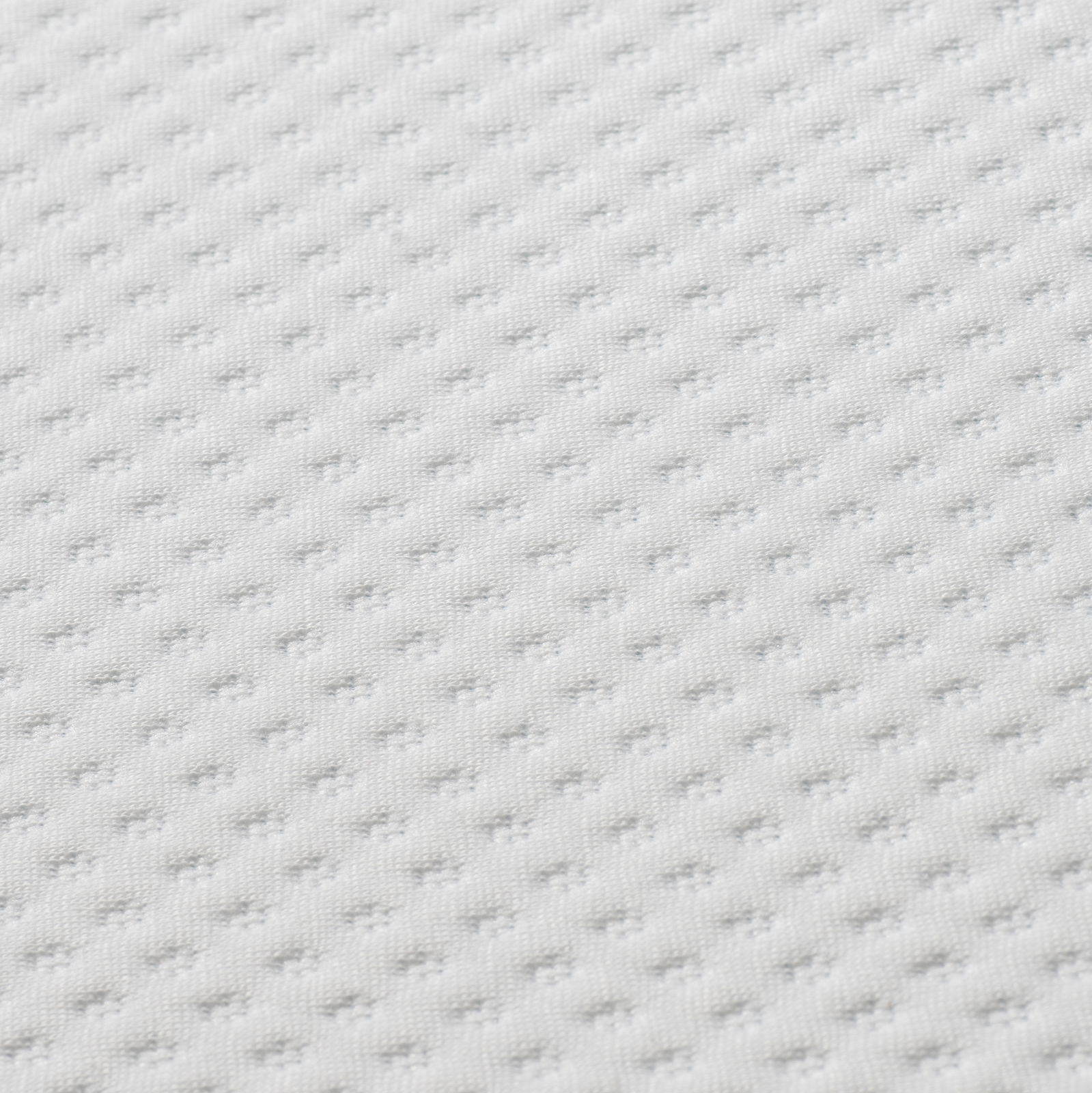 Nahaufnahme eines weißen, strukturierten Matratzentoppers in diagonaler Perspektive.