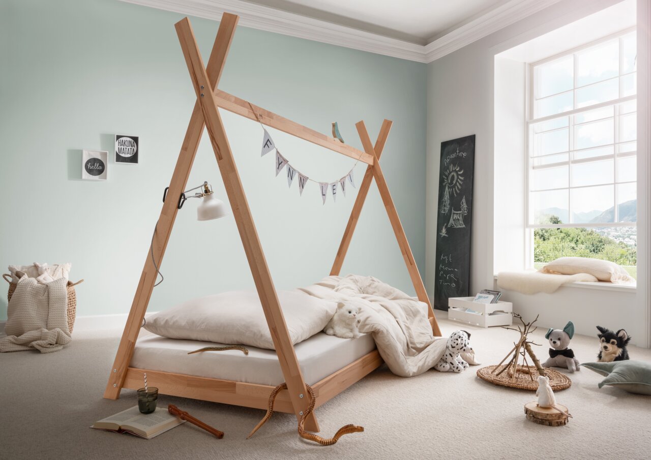 Tipibett aus Holz in einem hellen Kinderzimmer mit Dekorationen und Spielzeug, seitliche Perspektive