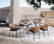 Moderne Gartenmöbelgarnitur mit einem rechteckigen Tisch und vier Stühlen aus Rattan, umgeben von einem Paravent, in einer stilvollen Außenumgebung. Perspektive von schräg oben.