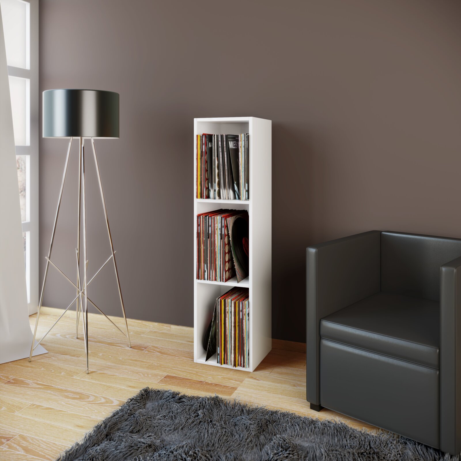 Weißes, schmales Schallplattenregal mit drei Fächern, gefüllt mit Vinyls, in moderner Wohnzimmerecke neben schwarzem Sofa und Stehlampe, Frontansicht in leichter Seitenperspektive.