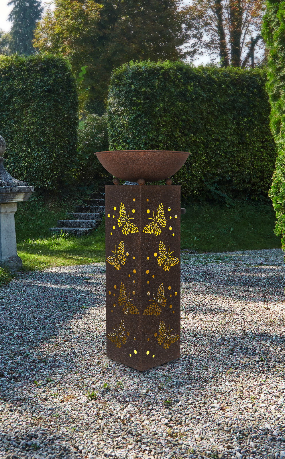 Rostfarbene Solarleuchte mit Schmetterlingsmuster, im Garten auf Kiesboden stehend, aus frontaler Perspektive fotografiert.