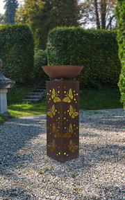 Rostfarbene Solarleuchte mit Schmetterlingsmuster, im Garten auf Kiesboden stehend, aus frontaler Perspektive fotografiert.