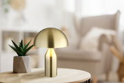 Moderne Tischleuchte ATOMA in Goldoptik auf einem Holztisch, seitliche Perspektive
