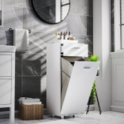 Weißer Badezimmer-Wäscheschrank mit ausklappbarem Wäschekorb und Schublade, leicht schräg von vorne rechts fotografiert, im modernen Bad mit grauen Fliesen und rundem Spiegel.