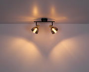 Zweiflammiger Strahler aus Metall in Schwarz und Gold, an der Decke montiert, mit warmem Lichtschein.