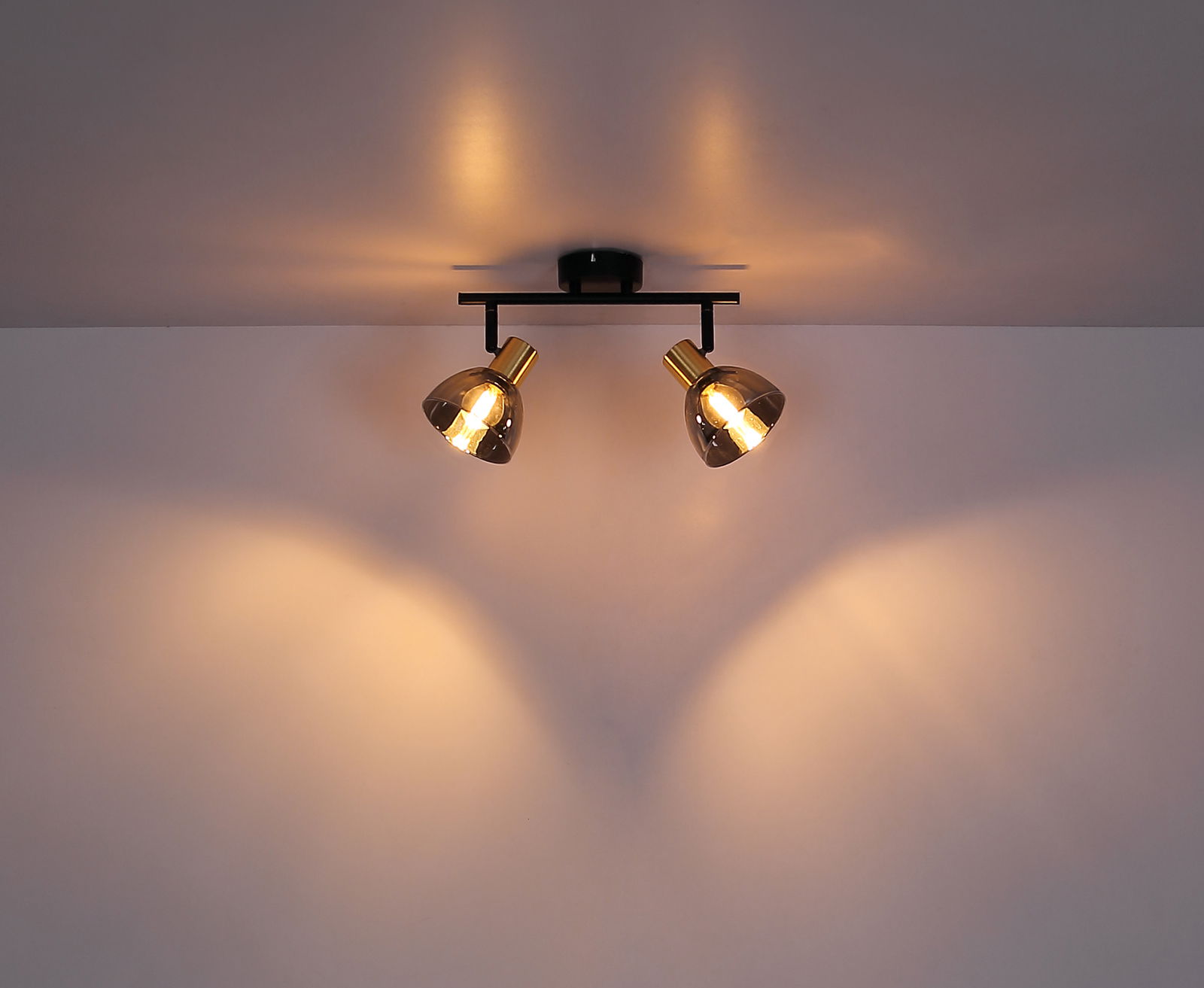 Zweiflammiger Strahler aus Metall in Schwarz und Gold, an der Decke montiert, mit warmem Lichtschein.