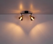 Metalen spot met twee lampen in zwart en goud, aan het plafond gemonteerd, met een warme lichtuitstraling.