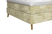 Nahaufnahme eines Boxspringbettes 180x200 mit beigem Stoffbezug und Holzfüßen, seitliche Perspektive.