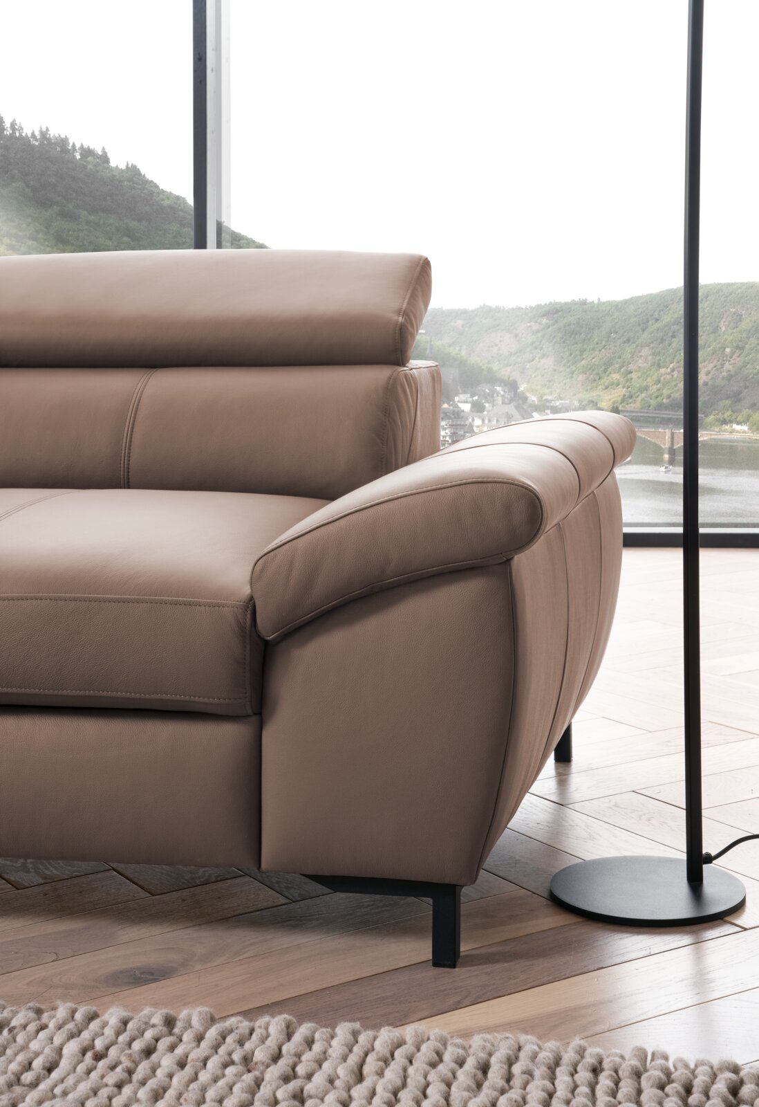 Nahaufnahme einer braunen Ledercouch mit Armlehne und verstellbarer Kopfstütze, seitliche Perspektive.