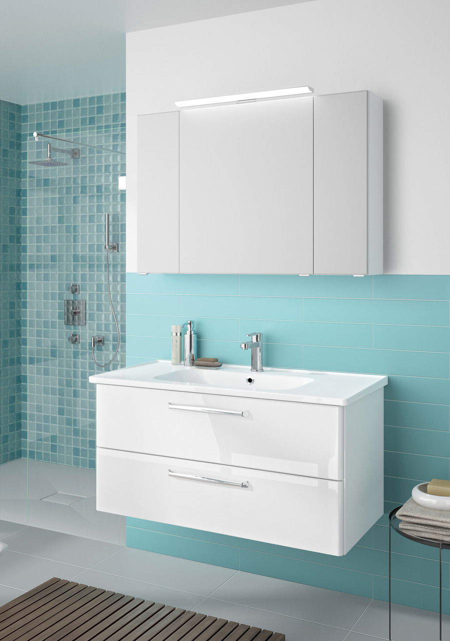 Moderner Badblock mit weißem Waschbecken und Schubladen, vor türkisfarbenen Fliesen, aus der Perspektive von vorne rechts.