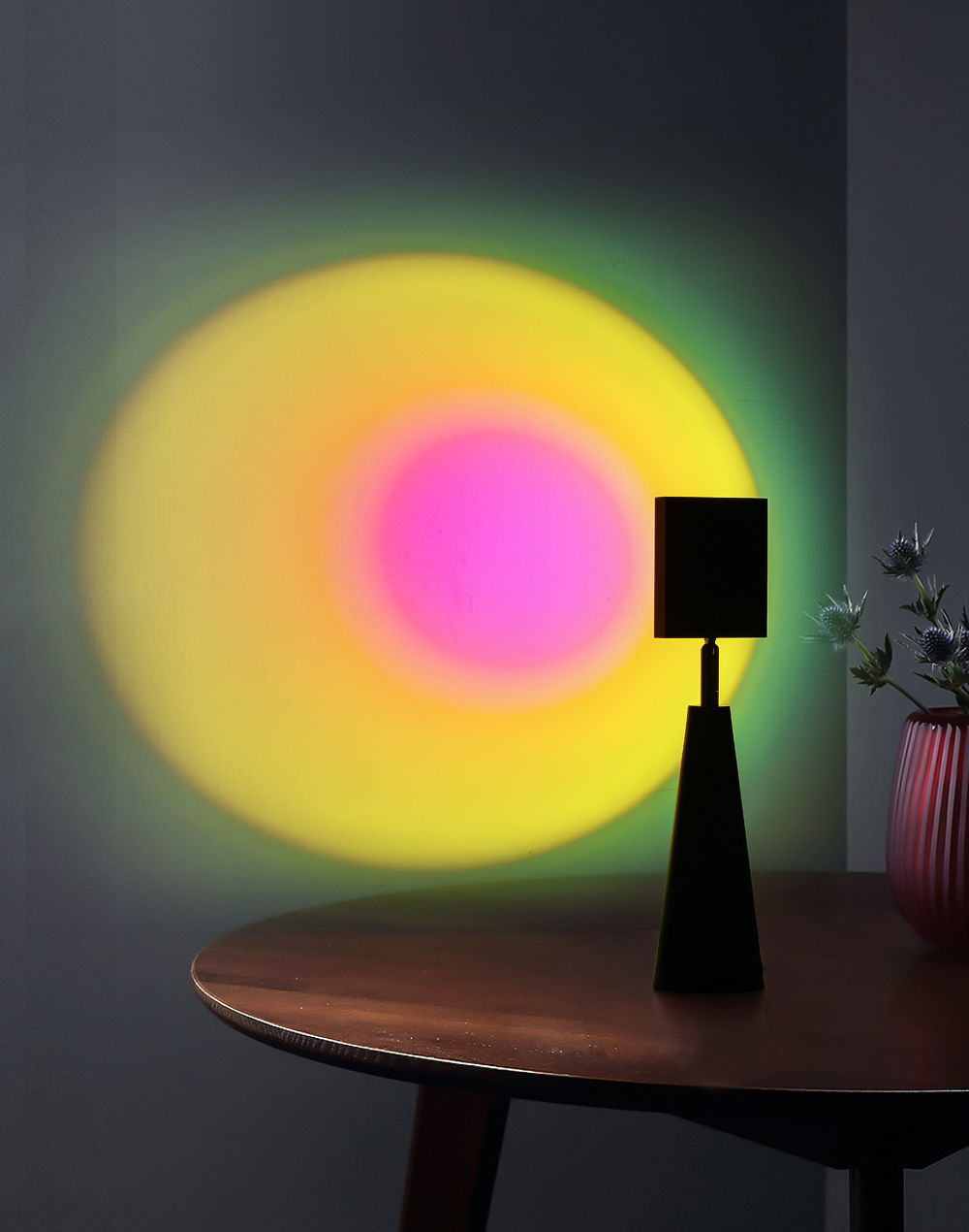 Tischleuchte Ryusei auf einem Tisch, die bunte Lichteffekte an die Wand projiziert. Perspektive von der Seite.