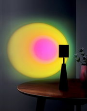 Tischleuchte Ryusei auf einem Tisch, die bunte Lichteffekte an die Wand projiziert. Perspektive von der Seite.